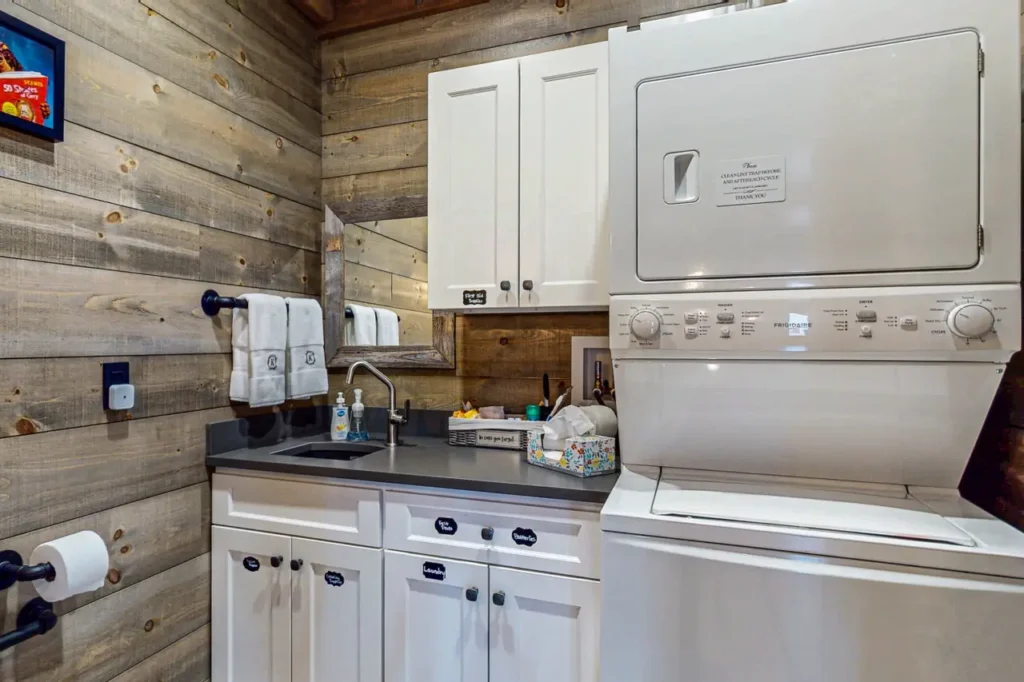Washer and dryer in a lodge laundry area with wooden walls, featuring towels, a sink, and cleaning supplies, highlighting convenience for guests at Kings Landing.