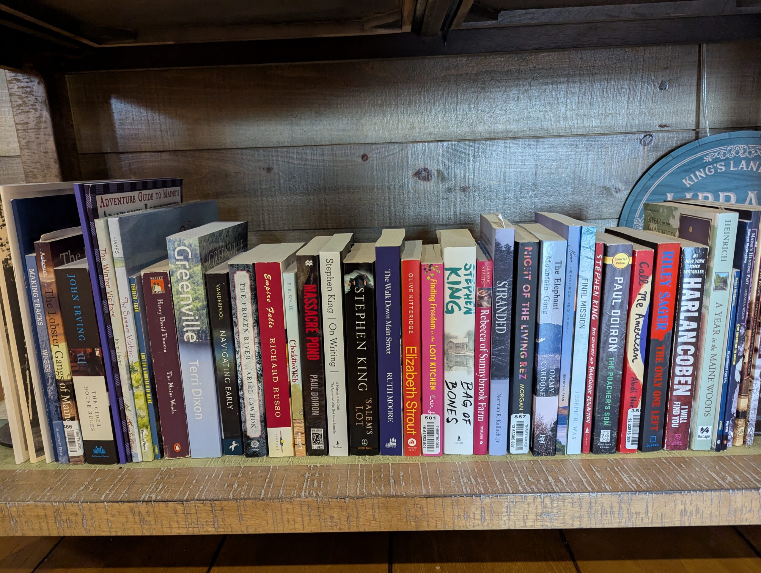 Books on a shelf in the Mainly Maine Library, featuring titles by Stephen King, local guides, and contemporary Maine authors, highlighting a cozy reading space for guests.